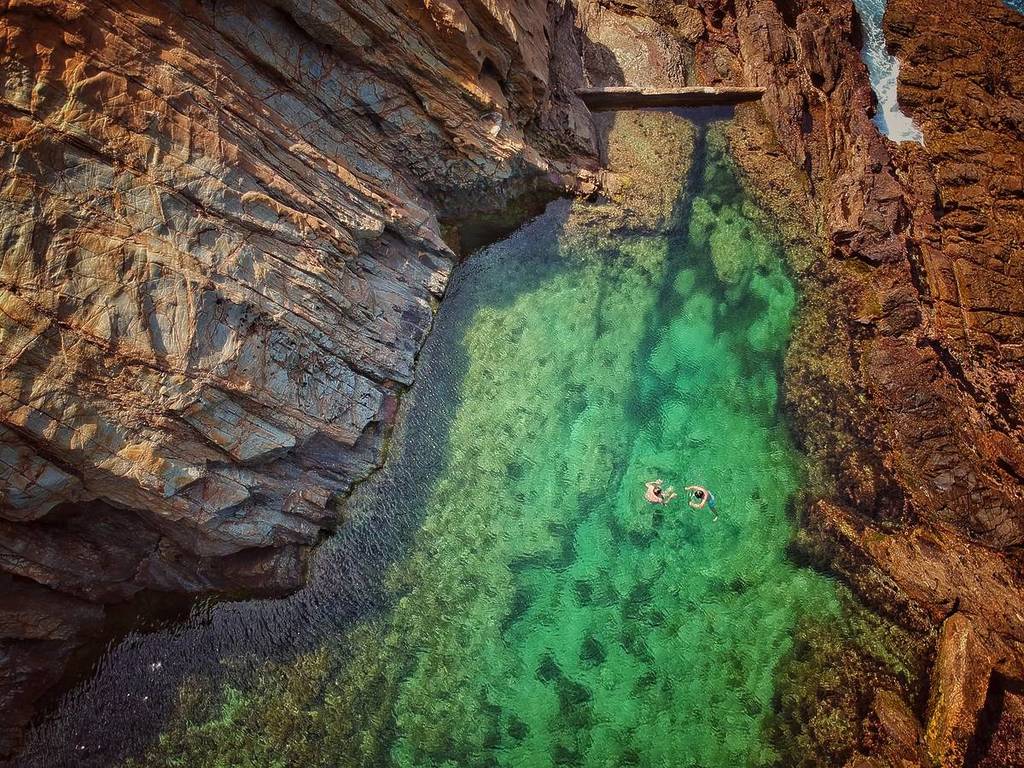 Aerial view of swimmers floating in the clear emerald water of the Blue Pool, surrounded by steep rock walls and natural rock formations