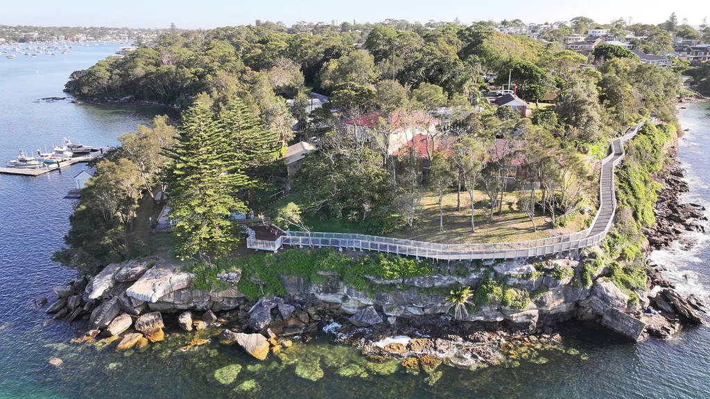 Wide aerial view of the Hungry Point Clifftop Walk curving along rugged cliffs, with clear water and rocky shoreline below