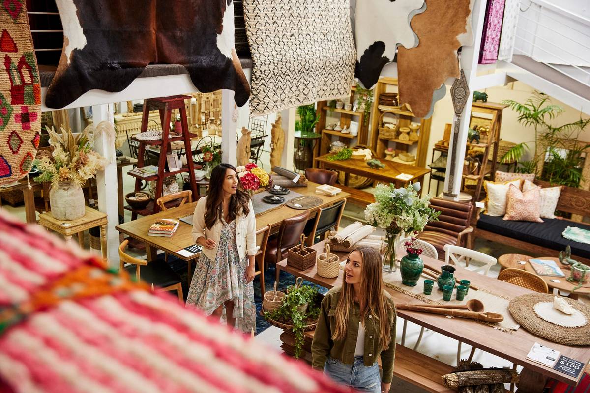 Two women browsing a boho-style homewares store with wooden furniture, woven rugs and natural decor in Bellingen NSW