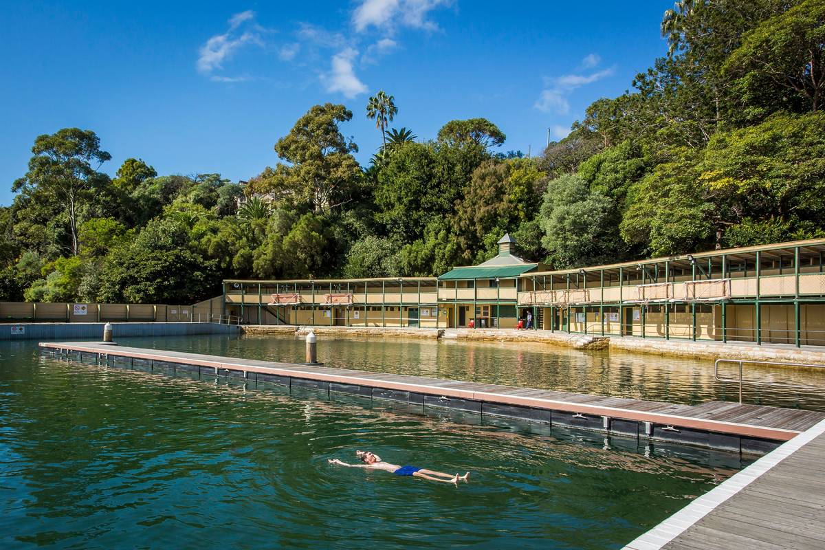 A swimmer floating in Australia’s oldest swimming pool in Sydney, surrounded by heritage buildings and bushland