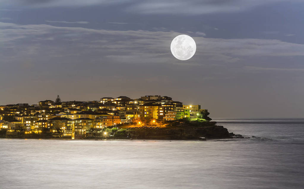 Full Snow Moon rising over a coastal suburb at night in Australia