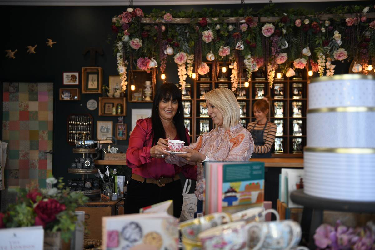Two women sharing a teacup inside a charming tea shop in Berry, NSW, with floral decor and shelves of teas behind them