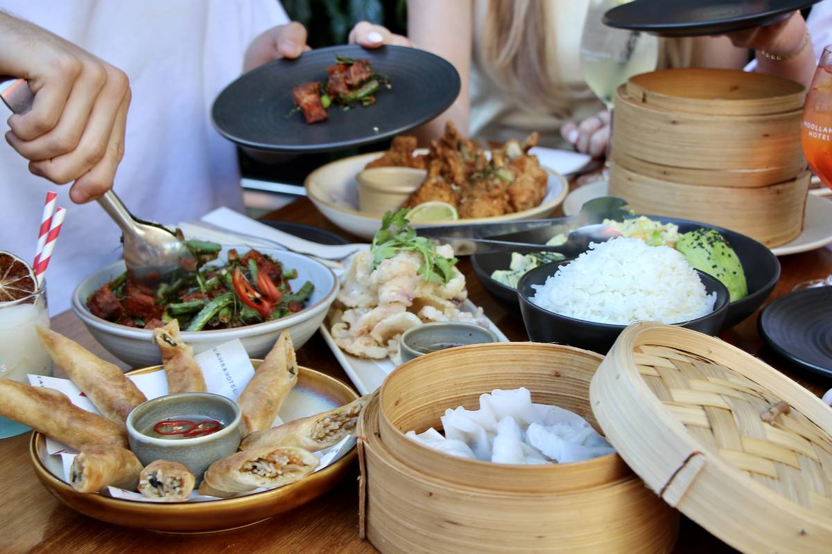 Shared Pan-Asian dishes on a table, including dumplings, spring rolls, rice bowls and cocktails