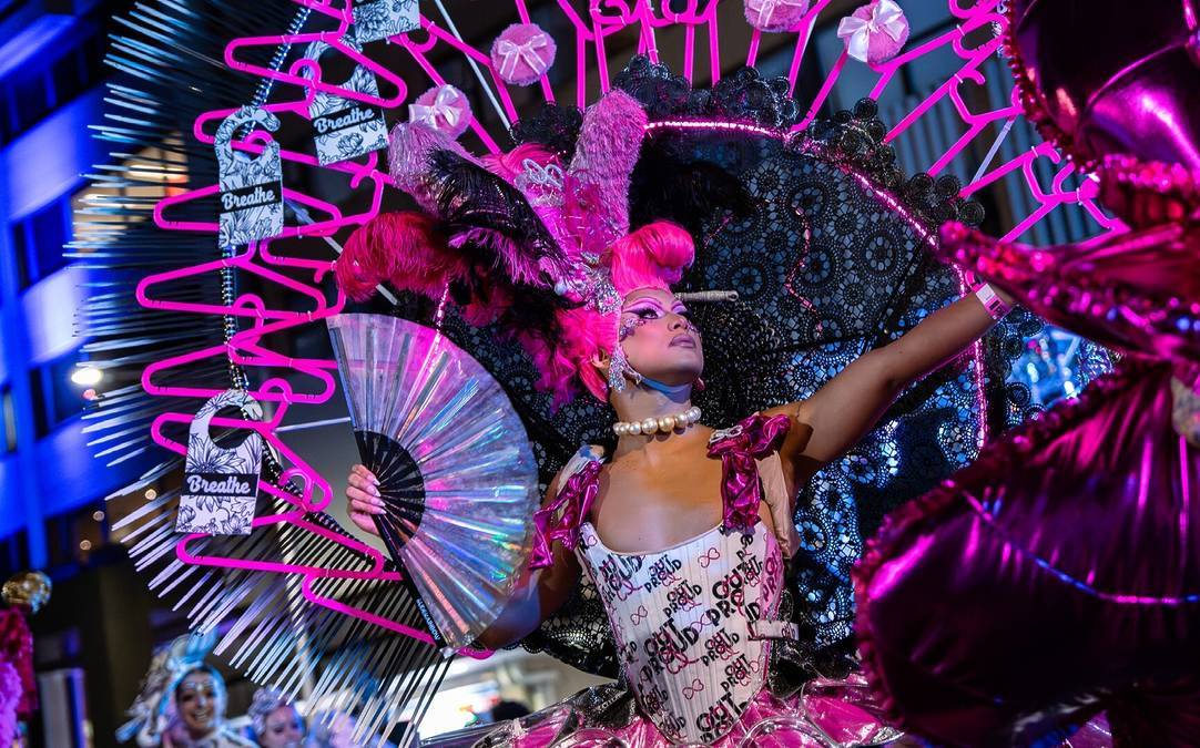 Mardi Gras parade performer in a pink costume with feathers and fan, dancing under bright lights