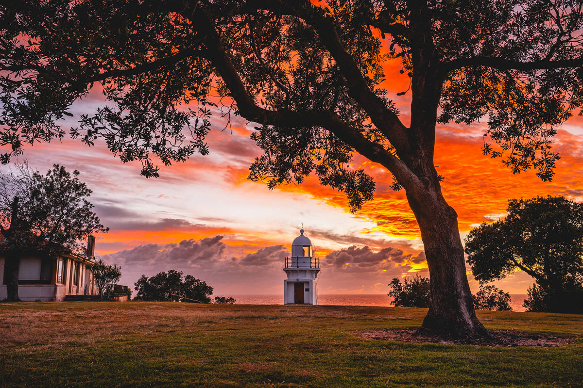 White lighthouse on a grassy headland at sunset with orange sky and ocean in the background in NSW