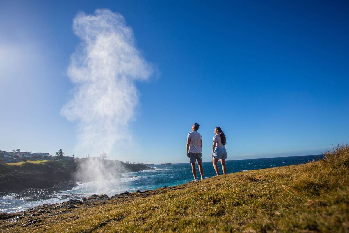 Couple watching the Kiama Blowhole erupt along the rugged South Coast coastline in NSW