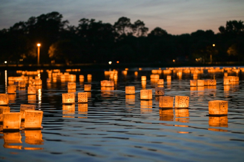 Dozens of glowing water lanterns floating across a lake at night