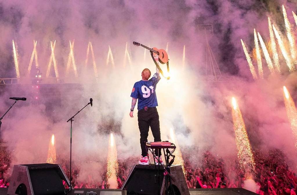 Ed Sheeran raising his guitar on stage as fireworks light up the crowd for his Loop stadium tour