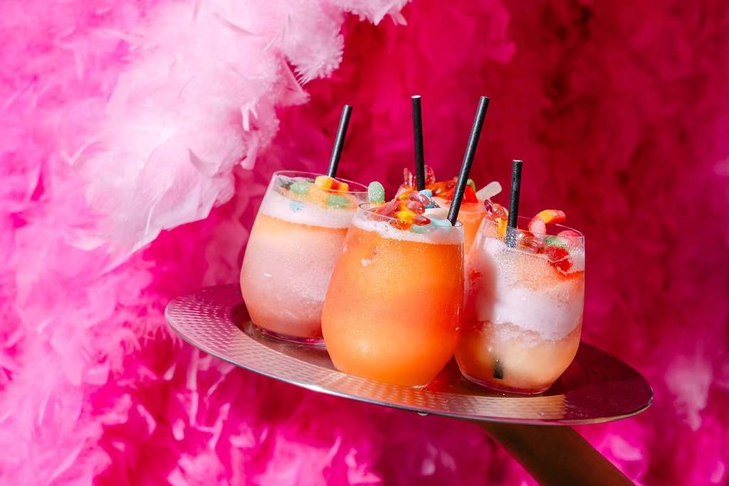 A tray of colourful cocktails set against a background of pink feathers.