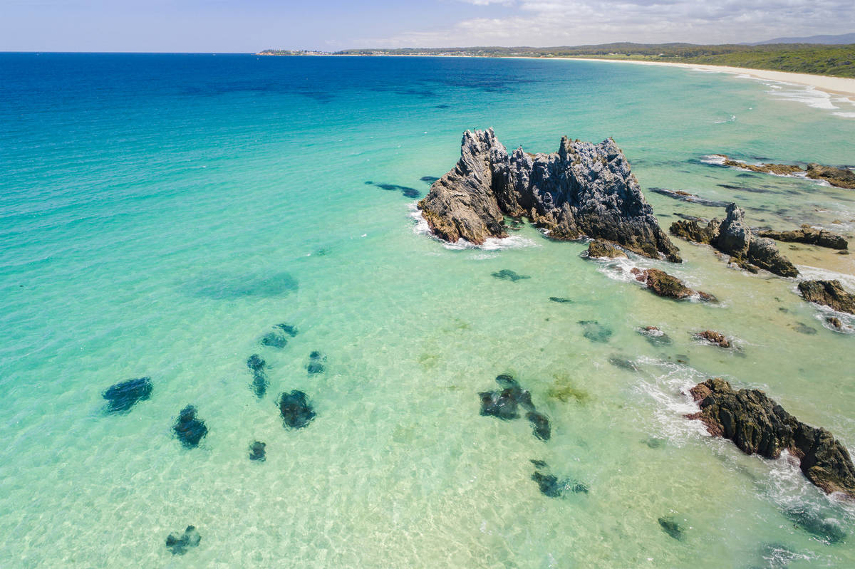 Aerial view of Camel Rock rising from clear turquoise water off the Bermagui coastline