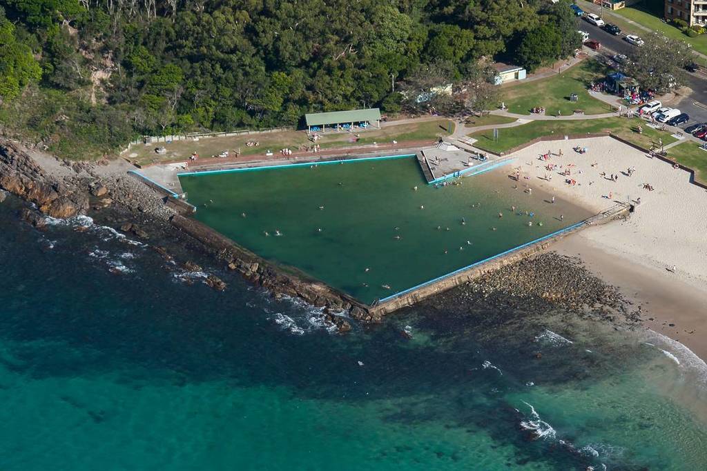 Aerial view of the Forster Ocean Baths, a large ocean-fed rock pool set beside the beach with turquoise water and swimmers