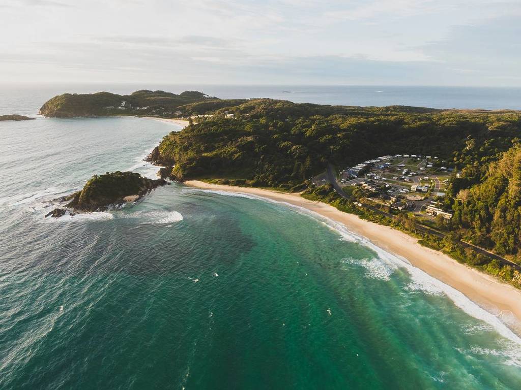 Aerial view of a secluded beach and headland with turquoise water and coastal campground at Seal Rocks