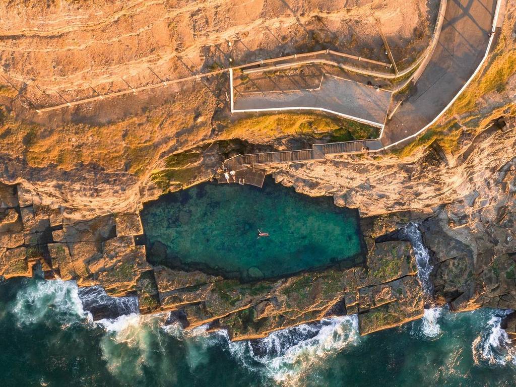 Aerial view of Bogey Hole in Newcastle, showing the historic ocean pool carved into the rock platform with clear blue water