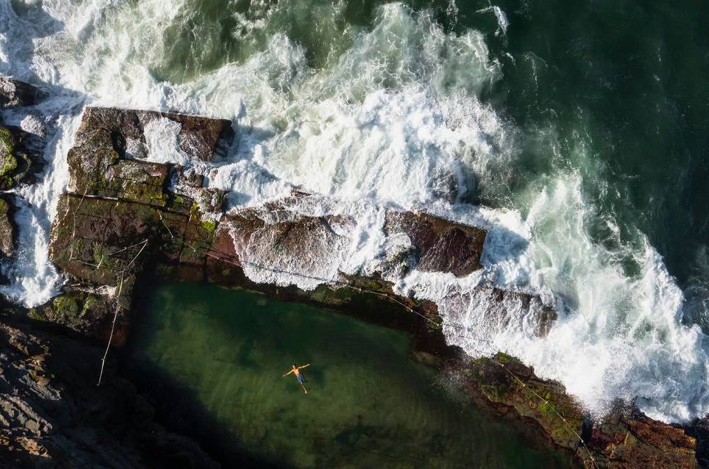 Aerial view of waves crashing over the Bogey Hole ocean pool in Newcastle, showing the rugged coastal rock platform