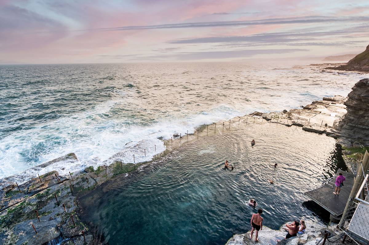 Bogey Hole ocean pool in Newcastle at sunset, with swimmers in the historic rock pool and waves breaking along the coastline