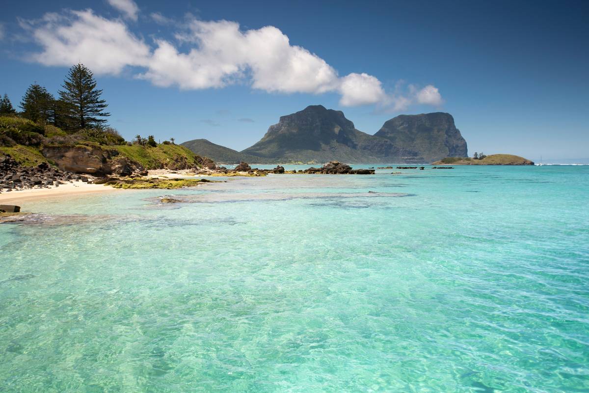 Crystal-clear turquoise waters in Lord Howe Island with volcanic peaks in the distance