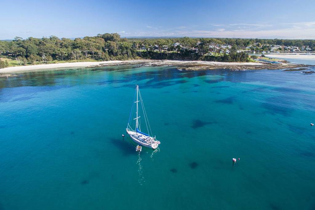 A sailboat floating in clear turquoise water near a quiet coastal bay in New South Wales