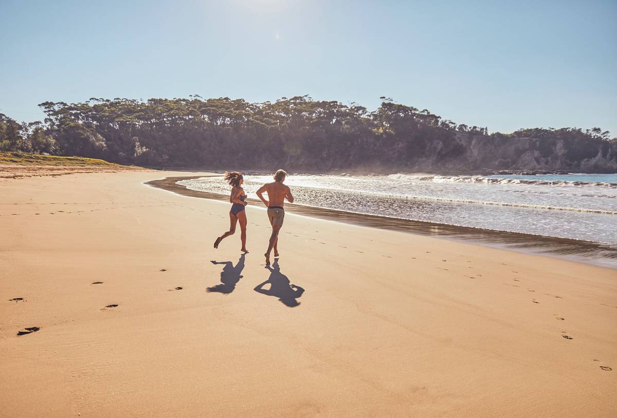 Two people jogging along a wide sandy beach on the NSW coast with waves rolling in