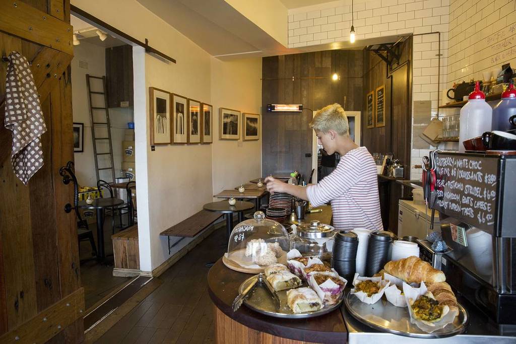 Barista preparing coffee beside pastries and baked goods inside a cosy cafe in the Blue Mountains