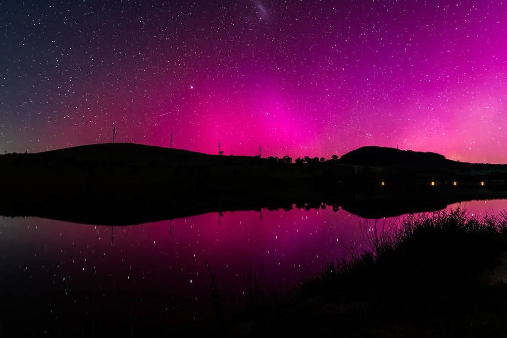 Vivid pink aurora lighting up the night sky above silhouetted hills and water