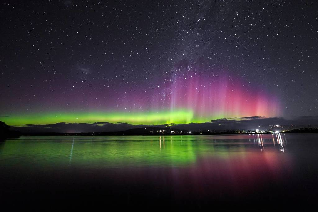 Aurora Australis glowing green and pink over calm water beneath a star-filled night sky