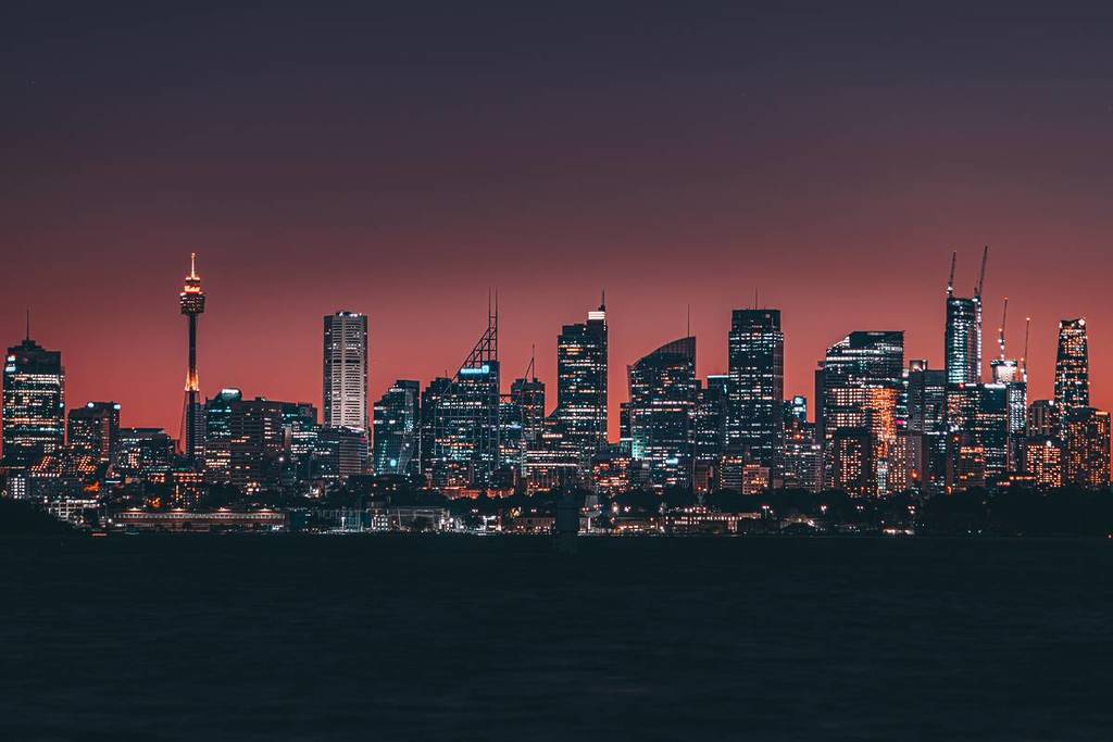 Sydney city skyline at dusk with illuminated buildings and deep orange sky over the harbour