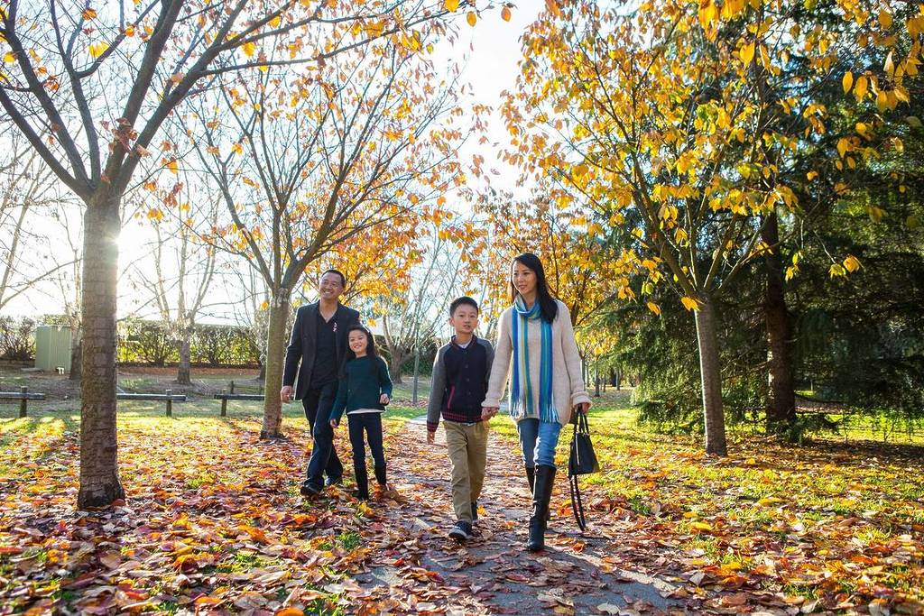 Family walking along a tree-lined path covered in autumn leaves in the Southern Highlands