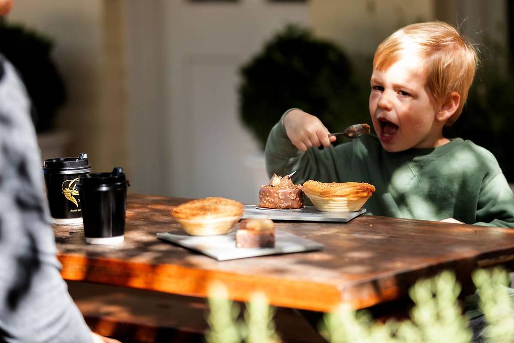 Child enjoying pastries and coffee at an outdoor table in Bowral on a sunny autumn day
