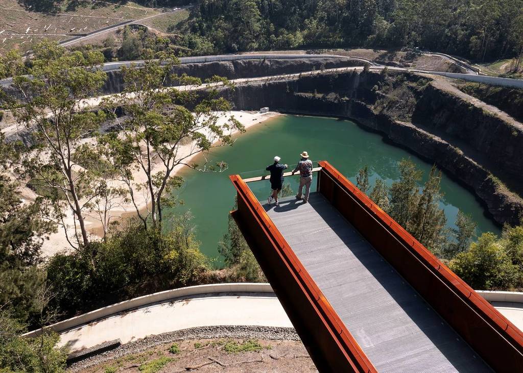 Two people standing on a lookout platform overlooking a former quarry with green water and steep rock walls at Hornsby Park