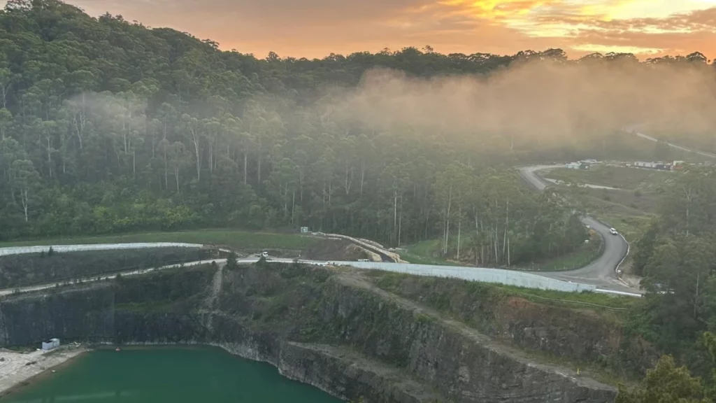 Wide view of a former quarry surrounded by bushland with winding roads at sunset