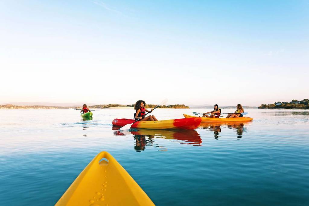 People kayaking on calm waters at Lake Macquarie during golden hour