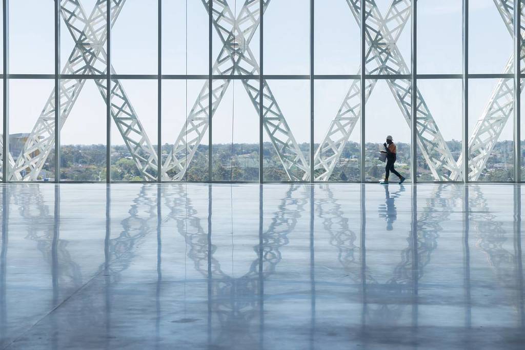 Interior view of Powerhouse Parramatta with large glass walls, structural lattice framing and a worker walking across the open exhibition space
