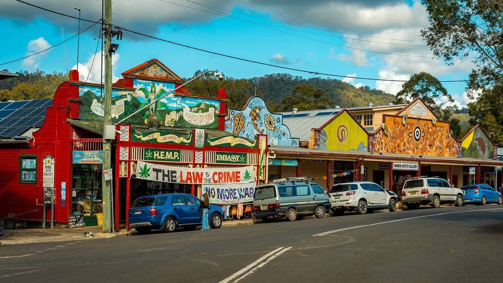 Colourful mural-covered buildings along Nimbin’s main street in NSW, with parked cars and surrounding hinterland hills in the background