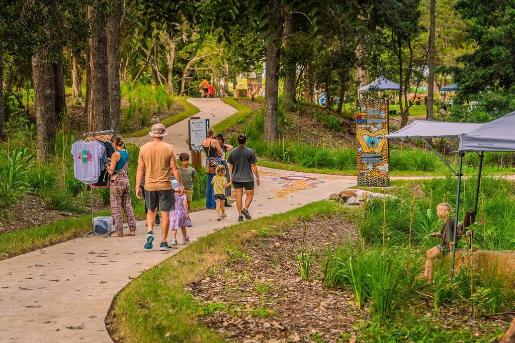 Visitors walking along a tree-lined path in a park near Nimbin, surrounded by greenery and open space.