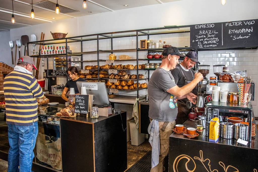 Busy local cafe in Armidale with baristas making coffee and shelves of fresh bread