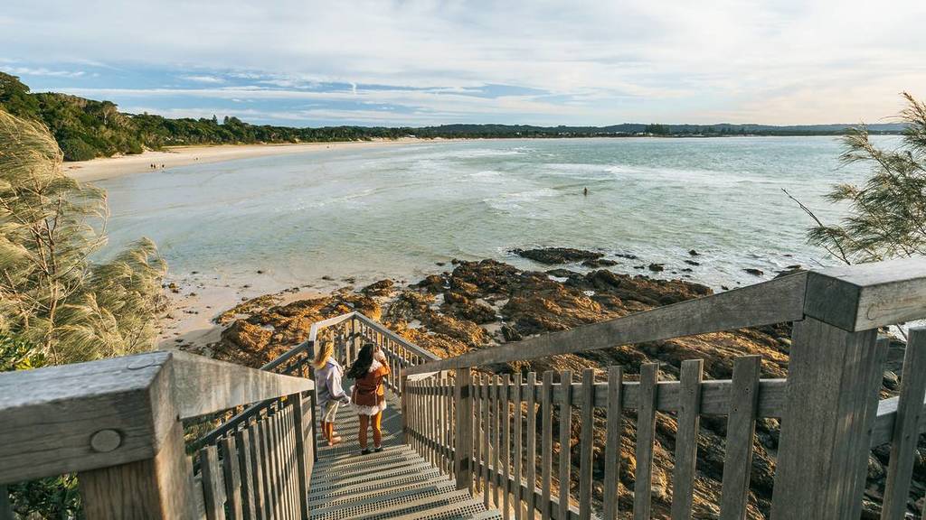 Coastal staircase leading down to a quiet beach in Byron Bay with sweeping ocean views and rocky shoreline