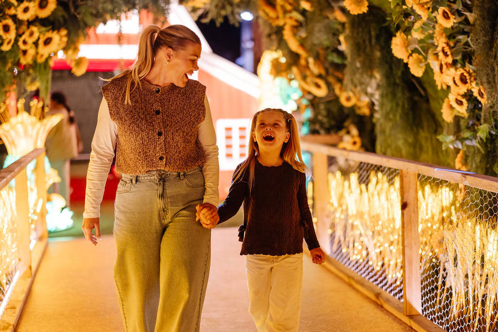 Mother and daughter walk through a sunflower-lined illuminated tunnel at the Lightfields winter attraction in Sydney