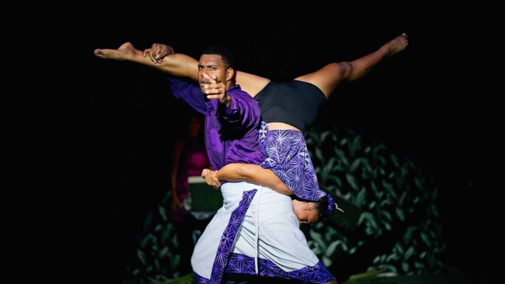A man and a woman dressed in purple, black and white costumes perform an acrobatic stunt at the Fijian Flying Circus Tour.