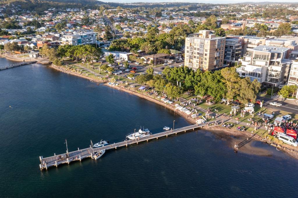 Aerial view of the new public wharf at Belmont on Lake Macquarie, with boats moored alongside the jetty and people gathered along the waterfront foreshore