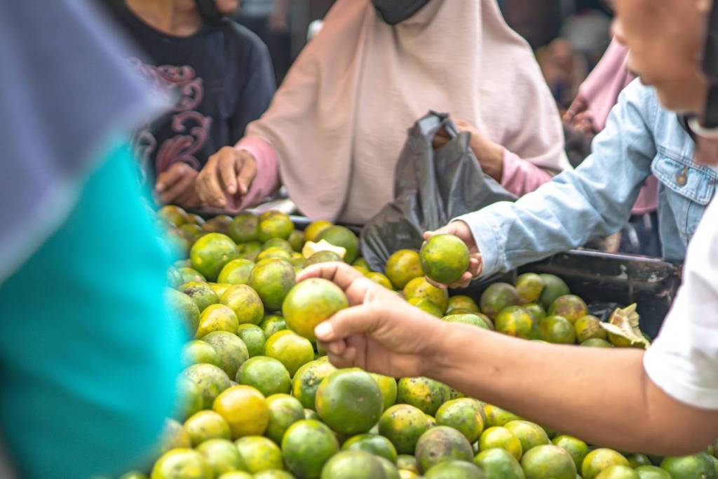 People picking out sweet oranges from a crate full of fruit
