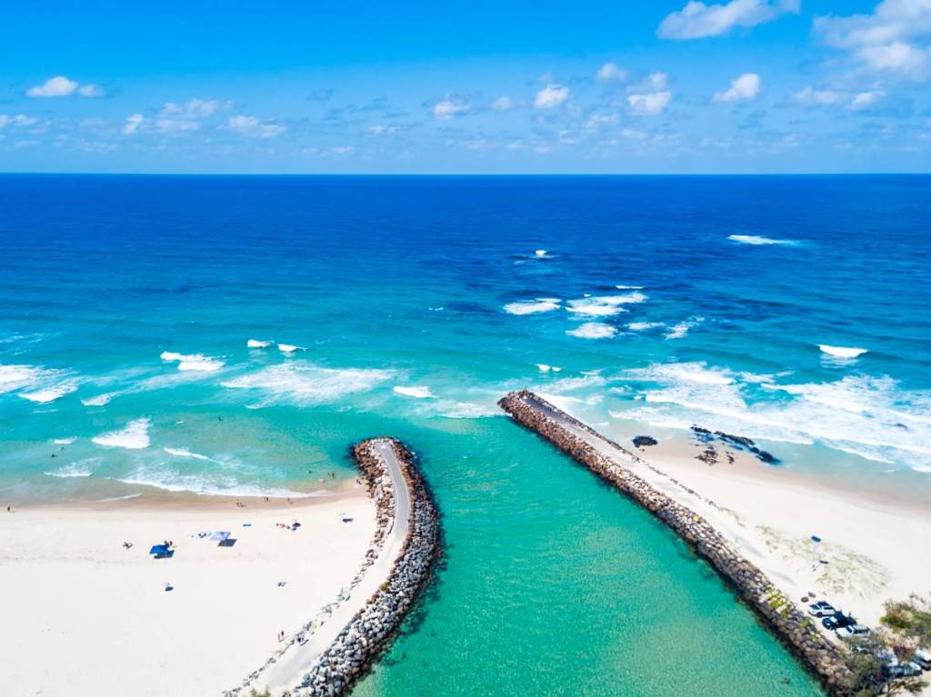 Aerial view of turquoise water flowing between sandy beaches into the ocean at Kingscliff