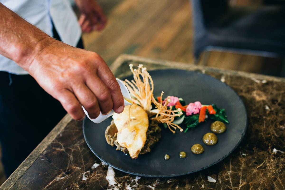A chef pours sauce over a carefully plated seafood dish at a restaurant in Kingscliff