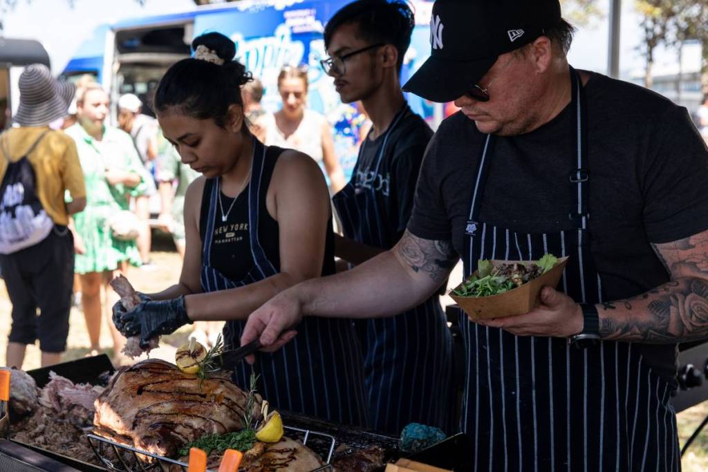 Food vendors carve roasted meat and serve customers at a busy outdoor market stall