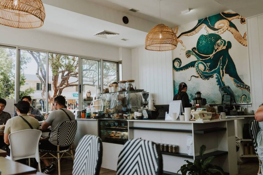 Interior of a Vincentia cafe with diners, wicker pendant lights and a large octopus mural behind the counter