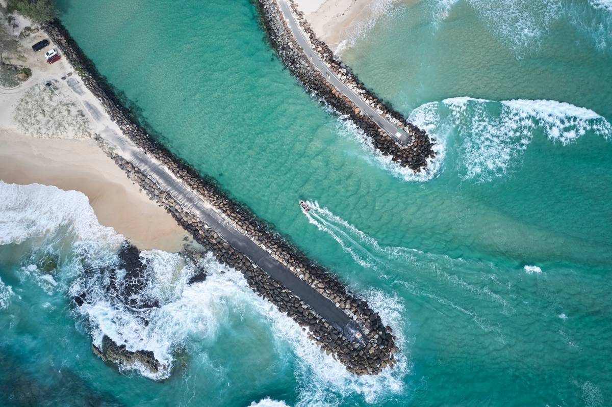 Aerial view of turquoise water and rock breakwalls at the mouth of Cudgen Creek in NSW