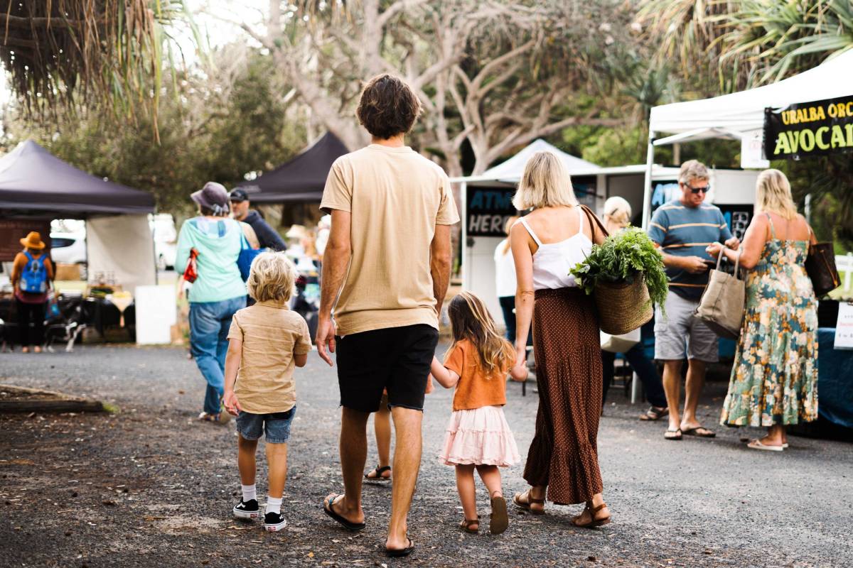 Family walking through a bustling outdoor market in Yamba, NSW, with fresh produce and local stalls