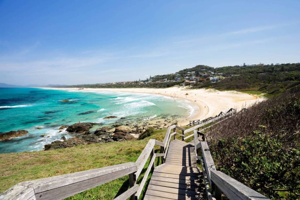 Wooden steps leading down to a sweeping sandy beach with bright turquoise waters along the Port Macquarie coastline