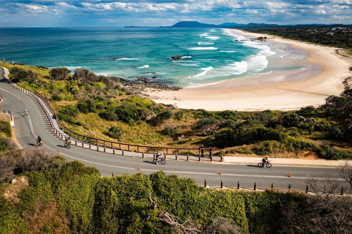 Elevated view of a sweeping sandy beach and turquoise ocean waters in Port Macquarie, with cyclists riding along the coastal road