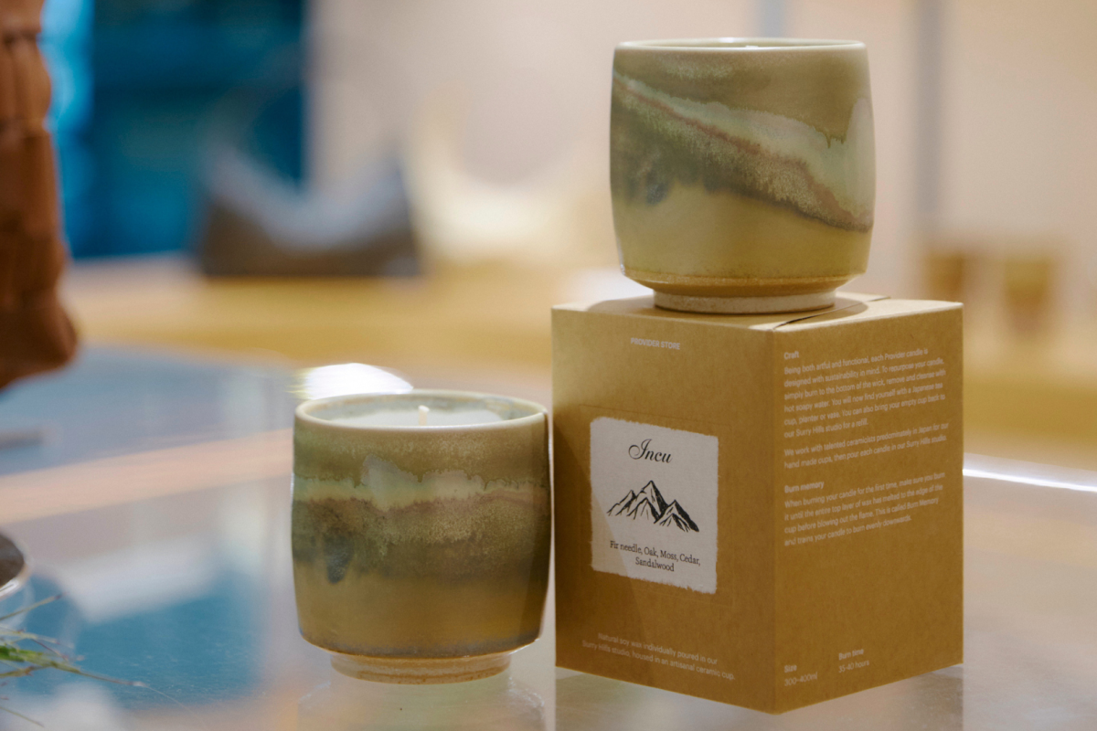 Two candles in green and brown ceramic vessels, including the Incu fragrance with notes of fir needle, oak moss, cedar and sandalwood