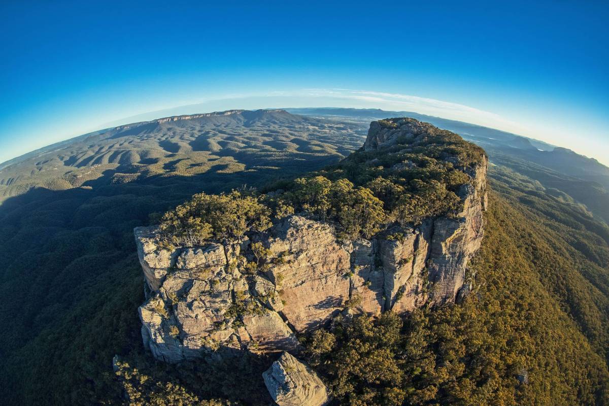 Wide-angle aerial view of massive sandstone cliffs overlooking the forested landscape of Capertee Valley